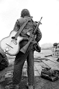 Carrying a guitar and a M16 rifle, a Marine waits at a landing strip for a flight out of Khe Sanh, February 25th, 1968
