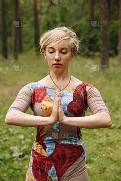 快乐的年轻女子站在瑜伽姿势在草地上的公园。在树的背景下练习瑜伽