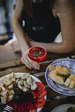 日落时分，一个穿着黑色t恤的女孩坐在桌边，手里拿着一杯鸡尾酒。奶酪和肉拼盘。切西瓜