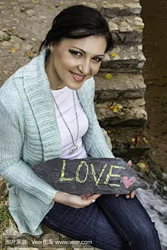 快乐的年轻女子，在一块石头上显示出爱情
Happy young woman showing the words, Love, on a stone