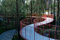 This may contain: a circular walkway in the middle of a park surrounded by trees and bushes with red railings