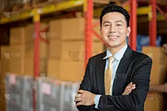 肖像年轻的亚洲人老板经理站在货架旁的产品箱在大仓库工厂商店，微笑和感觉快乐，物流进出口运输理念