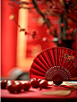 桌子上放着一把红色的折扇，旁边放着几颗红梅，背景比较模糊，好像在举行婚礼。中国的新年海报创造了一个独特的场景。春节气氛，喜庆，特写，高端，静物拍摄--ar 34-v 6 (50)