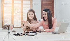美妆博主，两位美丽的亚洲女性正试图了解和销售化妆品。通过在线流媒体从相机和笔记本电脑带着一个快乐的笑