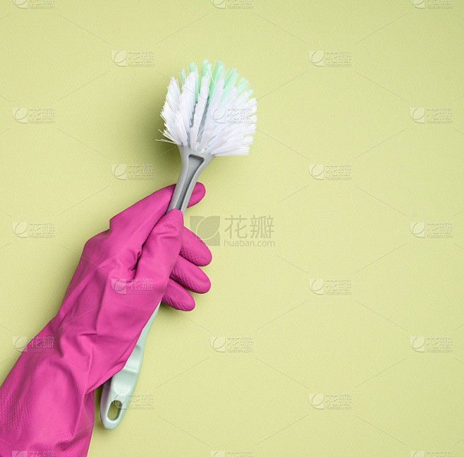 女性手在紫色橡胶手套握塑料清洁刷在绿色背...