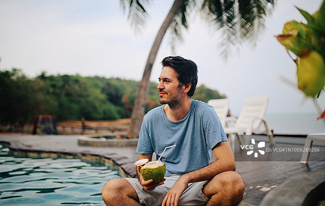 在泰国兰塔岛的海边，一个年轻人正在喝新鲜...