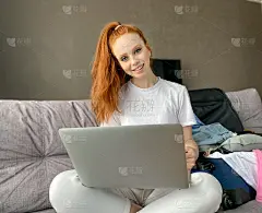 一个漂亮的女孩坐在沙发上，旁边是一个手提电脑，拿着一张信用卡购物