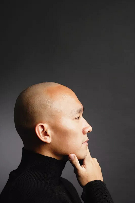 光头男子，手放在下巴上，看向别处图片