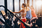 Three athletic people warming up on exercise machines in a gym.