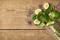 健康食品的概念。烹饪排毒奶昔的配料。玻璃上放有菠菜、香蕉、酸橙和奇异籽的木桌，可以俯视，复制空间