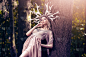 性感的白人女孩摆姿势的特写肖像与艺术的鹿角和长浅色连衣裙在夏季森林与光闪光在背景。水平的形象定位