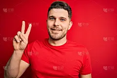 年轻男子与蓝色眼睛穿着休闲t恤在红色孤立的背景微笑与快乐的脸眨眨眼睛在相机做胜利标志。二号人物。