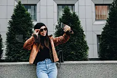 City style. Technology. Autumn/spring. Stylish girl in casual clothes is doing selfie using a smartphone and smiling while walking outdoorsCity style. Technology. Autumn/spring. Stylish girl in casual clothes is doing selfie using a smartphone and smiling