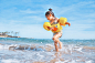 A little girl in yellow arm floats runs through small waves on a beach while giggling