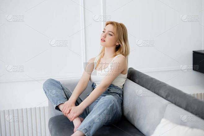 年轻的金发女人坐在沙发上，望着别处 