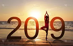 2019年新年贺卡。健康女孩的剪影在热带海滩上做瑜伽，以日落的天空为背景，看着日落，这是2019数字