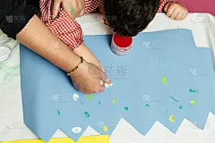 特殊教育的老师和学生穿着长袍，在桌子上用手画着生日花环和涂着丙烯颜料的黄色纸板。塑料工艺疗法。