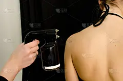 美容师手拿喷枪，在美容院用喷枪对穿着比基尼的年轻女性背部进行晒黑喷涂，在专业美容院用喷枪对女性身体进