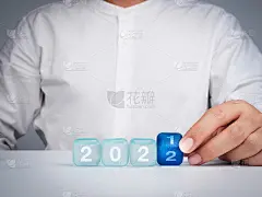新年快乐，2022背景概念。桌上的白色衬衫商人的特写手翻转蓝色方块，从2021年到2022年，现代简