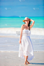 年轻美丽的女人在白色的热带沙滩上。白种女孩与帽子在背景的服装海