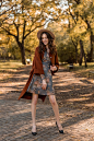 Attractive stylish smiling woman with curly hair walking in park dressed in printed dress and warm coat autumn trendy fashion, street style