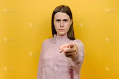 肖像严肃严格有吸引力的年轻白人女子20多岁穿着粉红色针织毛衣点食指相机在你激励命令做它，孤立在黄色背
