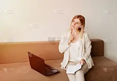 年轻的商务女性拿着笔记本电脑，坐在明亮的客厅里，望着窗外发呆