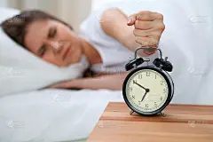 昏昏欲睡的年轻女子伸出手来敲响警钟，愿意关掉它。早醒、睡眠不足的概念