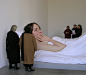 Ron Mueck，澳大利亚超现实主义雕塑家，1958年出生于墨尔本，现居英国，他自学艺术，早期事业是为电视和影片制作逼真的模型。作品为惊人的现实主义，他用玻璃纤维树脂材料做成的人体个个纤毫毕现，皮肤上毛发、皱纹、疤痕、青春痘应有尽有，皮下青筋若隐若现，栩栩如生，几乎令人听见呼吸，但同时，它们扭曲的形状又令人感到压抑窒息，具有心理上的震撼力。