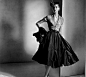 1952：Christian Dior日装 X形设计，采用较为挺括的绸缎面料，上衣是针织弹力纺织面料，所以整体效果更显得轻快和洒脱。上身是褶皱的V形开口领拼接在紧身的短上衣，腹部有抓褶，联排小包扣，以古典的方式展现现代的形体感，蓬松的裙摆与紧束的上衣形成戏剧化的对比，长及小腿中部的下摆体现摇曳的动感。挺括的海军式小礼帽上点缀着自然形态的布料褶花，使整套服装更有纵深感，从而增添了优雅气质。这是20世纪40年代女性的经典装扮。