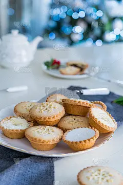 传统的英国节日糕点肉馅饼在茶点餐桌上，背景是点亮的圣诞树。舒适的心情回家。垂直的名片。特写，选择性聚