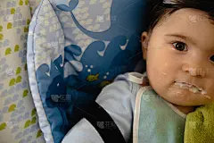 母亲在儿童座椅上喂她的婴儿儿子粥-亚洲混血的孩子男孩穿着蓝色的身体t恤与微笑熊卡通怀孕