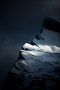 This may contain: the top of a mountain with snow on it's sides and dark clouds in the background