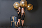 Free photo full-length portrait of dreamy female model with curly hairstyle holding party balloons in her room. indoor photo of pleased girl wears black dress and standing near blue gift box.