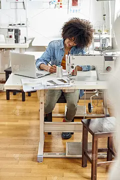 快活的非裔美国女性裁缝靠近现代笔记本电脑坐在工作场所