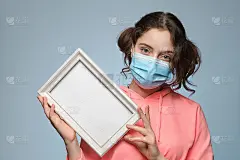 一个带着医用口罩，手里拿着相框的女孩。有一个刻铭文的地方。