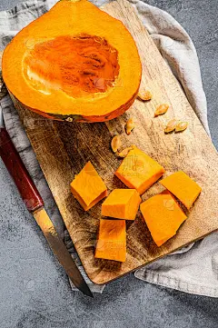 生南瓜放在砧板上，切成小方块。灰色的背景。美味健康的食物。南瓜种子。素食