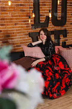 年轻女子坐在靠砖墙的沙发上说着情话。