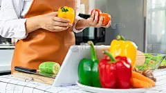 快乐的亚洲女性烹饪健康的食物，同时在阁楼厨房的平板电脑上寻找食谱，浏览烹饪课程导师网站，健康的食物和
