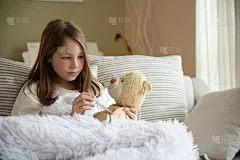 可爱的生病女孩测量泰迪熊的热度。