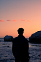 silhouette of man standing in beach watching orange sky over sea at dusk