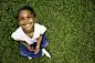 Portrait of adorable African American girlBeautiful preschool age African American little girl smiles while looking up at the camera. She is sitting in green grass.