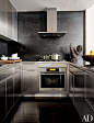 A folk-art rooster from the 1800s overlooks a modern New York City kitchen designed by Robert Passal. The cabinets are made of stainless steel, and the space is equipped with a Miele oven, cooktop, and hood.