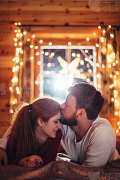 All I want for Christmas is youCouple lying on cozy bed in wooden cabin. Wearing Christmas pajamas. Together enjoying in the warmth of their home for Christmas. Room is decorated with festive string lights. Austrian Alps. Evening or night with beautiful y