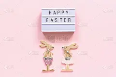 灯箱文字复活节快乐和一对木制兔子在粉红色的纸背景。概念复活节创意自上而下的组成平面躺贺卡
