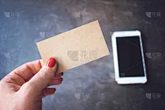 名片模型。女人手持回收纸空白名片散焦智能手机和笔记本背景。
