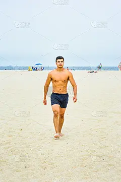 一个年轻的男子，半裸着，正在海滩上散步。