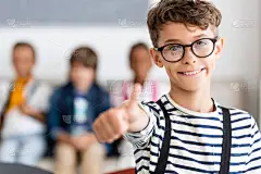 学生在眼镜中的选择性聚焦，在课堂上对着相机展示大拇指 