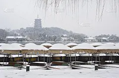 在杭州西湖的冬雪中，雷峰塔矗立在停泊的游船后面