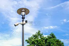 在公园的蓝色背景下，金属灯柱上的两个白色监控摄像头。